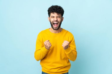 Faslı genç bir adam mavi arka planda izole edilmiş. Kötü bir durum yüzünden hayal kırıklığına uğramış.