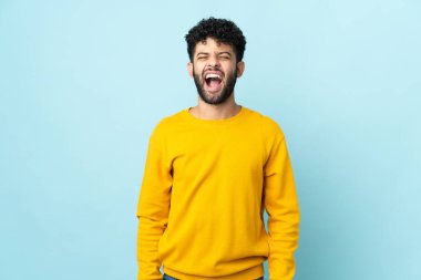 Faslı genç bir adam mavi arka planda izole edilmiş ve ağzı açık bağırıyor.