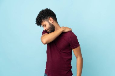Genç Faslı bir adam mavi arka planda izole edilmiş omuz ağrısından muzdarip.