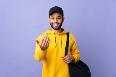 Spor çantalı genç Faslı sporcu, mor arka planda izole edilmiş, bizimle gelmesi için davet ediliyor. Gelmene sevindim.