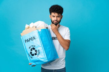 Genç Faslı bir adam, izole edilmiş arka plan üzerinde geri dönüşüm yapmak için elinde kağıt dolu bir geri dönüşüm çantası tutuyor.