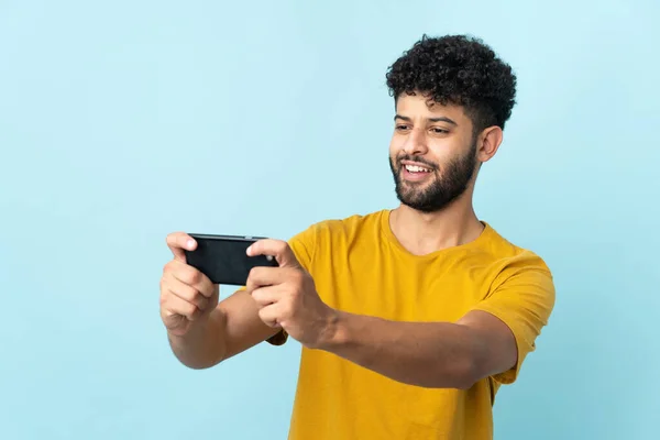 Young Moroccan man isolated on blue background playing with the mobile phone