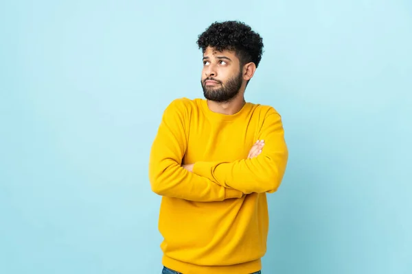 Young Moroccan man isolated on blue background making doubts gesture while lifting the shoulders
