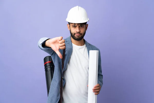 若い建築家モロッコ人ヘルメットと負の式で親指を示す隔離された背景の上に設計図を保持 — ストック写真