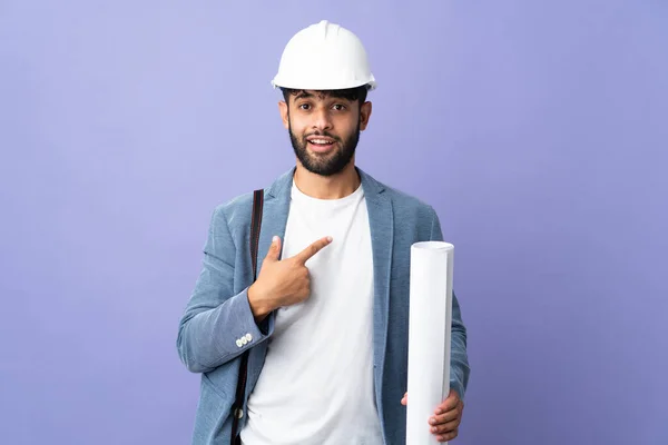 Young architect Moroccan man with helmet and holding blueprints over isolated background with surprise facial expression