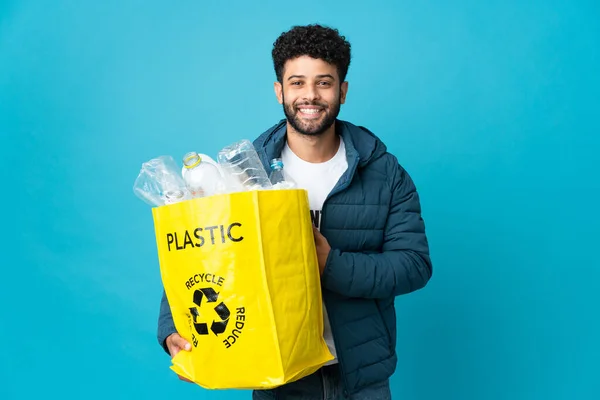 Young Moroccan man holding a bag full of plastic bottles to recycle over isolated background smiling a lot