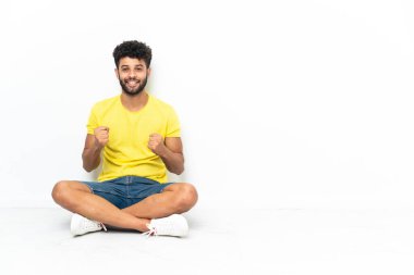 Genç Faslı yakışıklı adam izole bir zeminde oturmuş zaferi kutluyor.