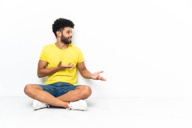 Genç Faslı yakışıklı bir adam yerde izole edilmiş bir şekilde oturuyor ve yüzünde sürpriz bir ifade var.