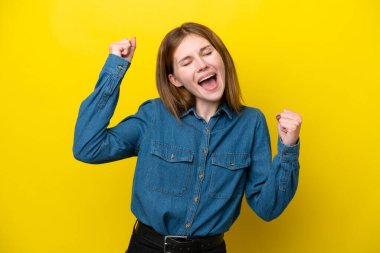 Sarı arka planda izole edilmiş genç İngiliz kadın zaferi kutluyor.