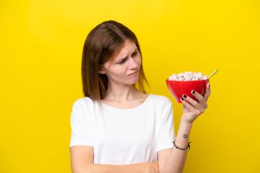 Sarı arka planda, üzgün bir ifadeyle izole edilmiş bir fincan kahve tutan genç İngiliz kadın.