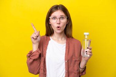 Sarı arka planda izole edilmiş bir şişe suyu olan genç İngiliz kadın çözümü bulmak için parmağını kaldırıyor.