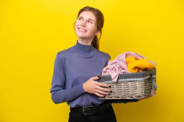 Young English woman holding a clothes basket isolated on yellow background thinking an idea while looking up