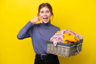 Young English woman holding a clothes basket isolated on yellow background making phone gesture. Call me back sign