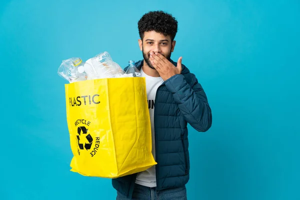 Young Moroccan man holding a bag full of plastic bottles to recycle over isolated background happy and smiling covering mouth with hand