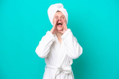 Bornozlu genç kadın mavi arka planda izole edilmiş bağırıyor ve bir şey duyuruyor.