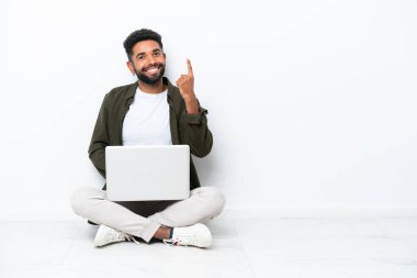 Yerde dizüstü bilgisayarı olan genç Brezilyalı bir adam işaret parmağıyla beyaz üzerine izole edilmiş olarak oturuyor. Harika bir fikir.