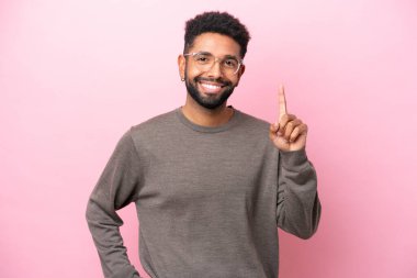 Pembe arka planda izole edilmiş genç Brezilyalı adam en iyinin işareti olarak parmağını kaldırıyor.