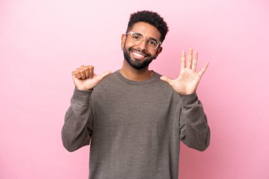 Pembe arka planda izole edilmiş genç Brezilyalı adam parmaklarıyla altısını sayıyor