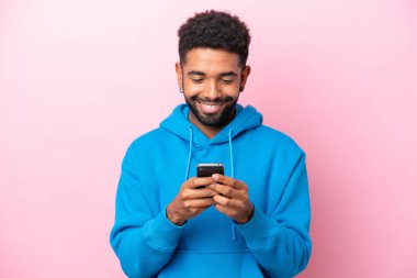 Pembe arka planda izole edilmiş genç Brezilyalı cep telefonuyla mesaj ya da e-posta gönderiyor.