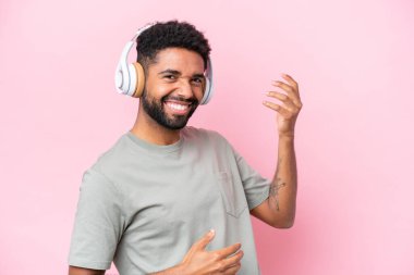 Genç Brezilyalı bir adam pembe arka planda izole edilmiş müzik dinliyor ve gitar hareketi yapıyor.