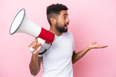 Young Brazilian man isolated on pink background holding a megaphone and with surprise facial expression