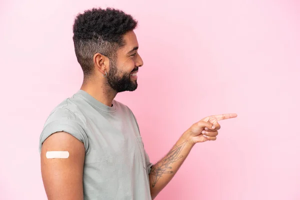Young Brazilian man wearing a band aid isolated on pink background pointing to the side to present a product