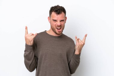 Beyaz arka planda izole edilmiş genç Brezilyalı adam boynuz hareketi yapıyor.