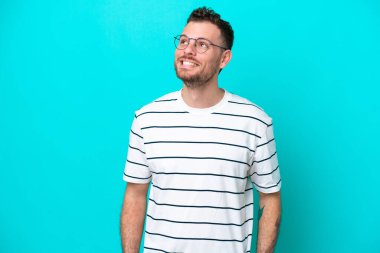 Genç Brezilyalı bir adam mavi arka planda izole edilmiş bir şekilde yukarı bakarken bir fikir düşünüyor.