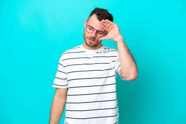 Genç Brezilyalı adam mavi arka planda izole edilmiş, yorgun ve hasta bir ifadeyle.