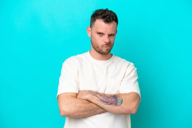 Genç Brezilyalı adam mutsuz bir ifadeyle mavi arka planda izole edilmiş.