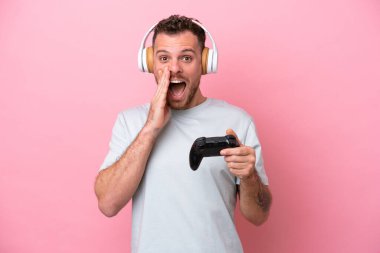 Young Brazilian man playing with video game controller isolated on pink background with surprise and shocked facial expression