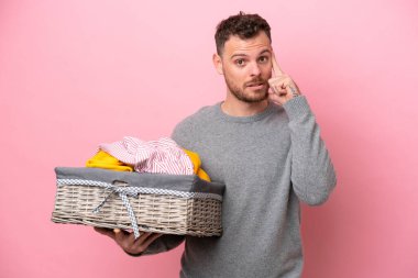 Genç Brezilyalı bir adam pembe arka planda izole edilmiş bir sepet tutarak bir fikir düşünüyor.