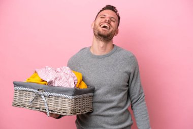 Genç Brezilyalı bir adam pembe arka planda izole edilmiş bir sepet tutuyor gülüyor.
