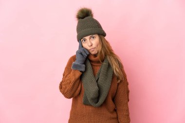 Kış şapkalı orta yaşlı bir kadın pembe arka planda izole edilmiş bir fikir düşünüyor.