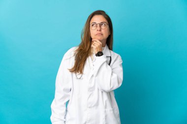 Orta yaşlı Brezilyalı doktor kadın mavi arka planda izole edilmiş ve araştırılıyor.