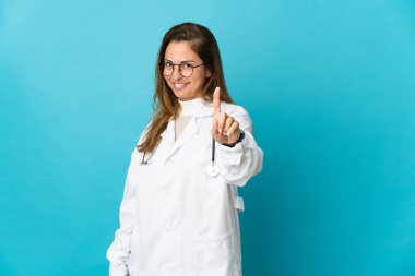 Orta yaşlı Brezilyalı doktor. Mavi arka planda izole edilmiş. Parmağını kaldırıp kaldırıyor.