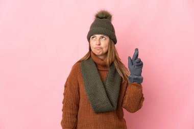 Kış şapkalı orta yaşlı kadın pembe arka planda izole edilmiş ve şans diliyor.