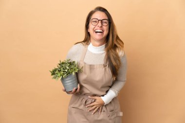 Orta yaşlı bahçıvan kadın elinde bej arka planda izole edilmiş bir bitki tutuyor.