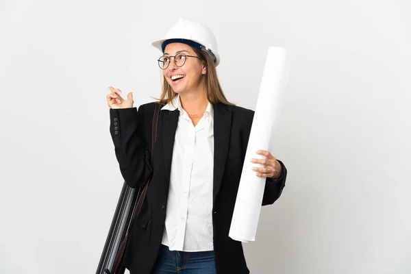 Middle age architect woman with helmet and holding blueprints over isolated background intending to realizes the solution while lifting a finger up