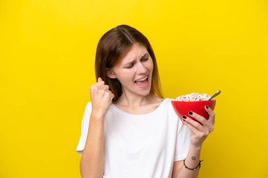 Sarı arka planda bir fincan kahve taşıyan genç İngiliz kadın zaferi kutluyor.