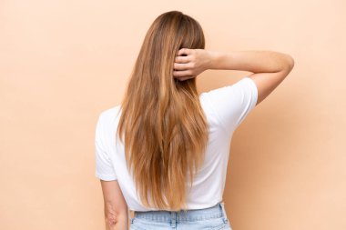 Beyazlı genç bir kadın arka planda bej bir arka planda izole edilmiş ve düşünüyor.