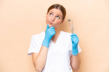 Beyaz dişçi kadının elinde bej arka planda izole edilmiş aletler var.