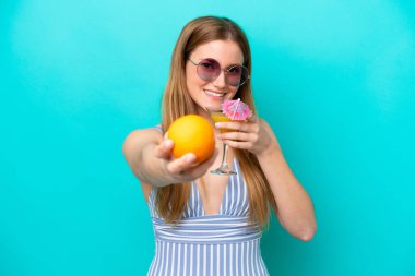 Mavi arka planda mayo giymiş ve elinde kokteyl tutan genç bir kadın.