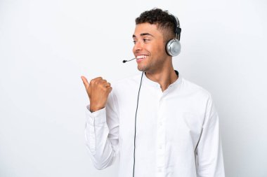 Tele pazarlamacı Brezilyalı beyaz arka planda izole edilmiş bir kulaklıkla çalışan bir adam bir ürün sunmak için kenarı işaret ediyor