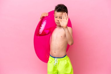 Küçük beyaz çocuk pembe arka planda izole edilmiş şişirilebilir bir çörek tutuyor. Durma hareketi yapıyor ve hayal kırıklığına uğruyor.