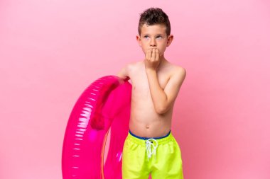 Küçük beyaz çocuk pembe arka planda izole edilmiş şişme bir çörek tutuyor. Şüpheleri var.