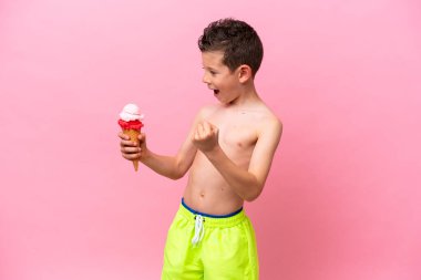 Pembe arka planda izole edilmiş dondurma yiyen küçük beyaz çocuk zaferi kutluyor.