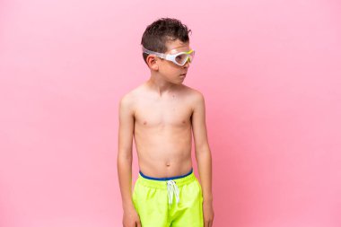 Pembe arka planda izole edilmiş dalış gözlüğü takan beyaz çocuk yan tarafa bakıyor.