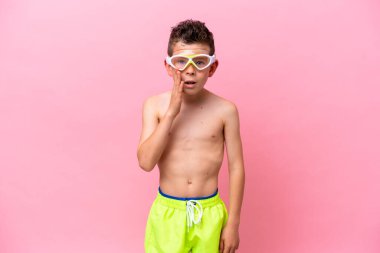 Pembe arka planda, şaşırmış ve şok olmuş bir yüz ifadesiyle izole edilmiş dalış gözlüğü takan beyaz bir çocuk.