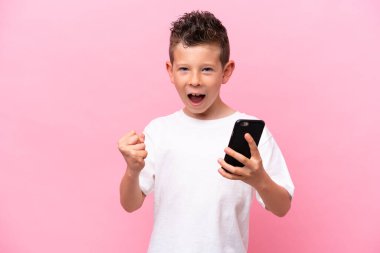 Pembe arka planda izole edilmiş, telefon zafer pozisyonunda küçük beyaz çocuk.